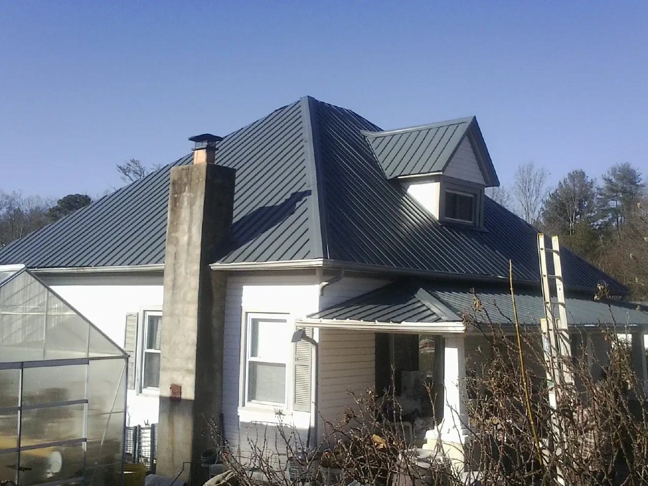 Dark blue standing seam metal roof on a white farmhouse with dormer — Slate & Tile Roof Repair by Roofing Brothers in Conneaut