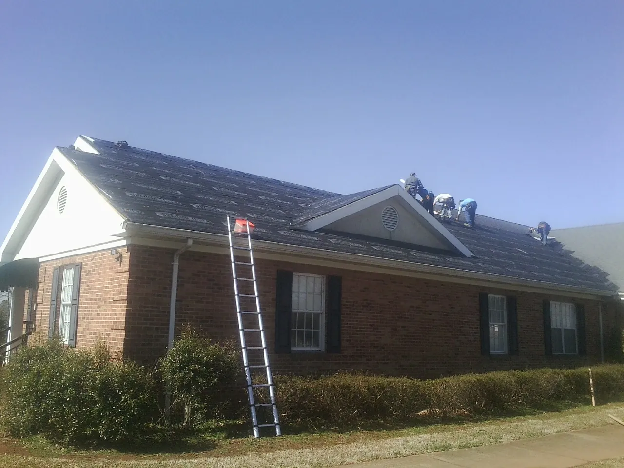 Crew tearing shingles off a brick ranch roof with a ladder set — Emergency Roof Repair work by our crew in Conneaut