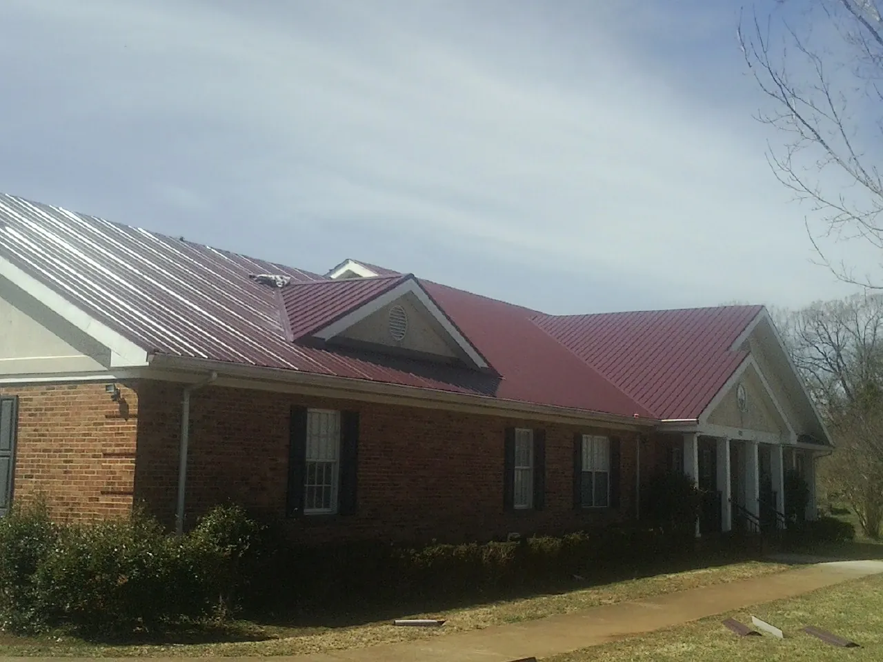 Red metal roof with gabled entries on a long brick building, from a Hail Damage Roof Repair job in Conneaut