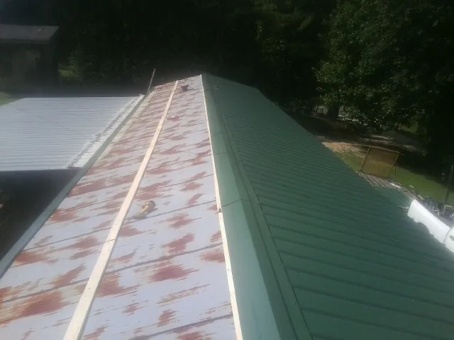 Old rusted panels beside newly installed green metal roofing — Wind Damage Roof Repair by Roofing Brothers in Conneaut
