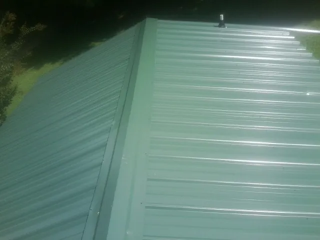 New green metal panels meeting at the ridge of a roof — Flat Roof Repair work by our crew in Conneaut