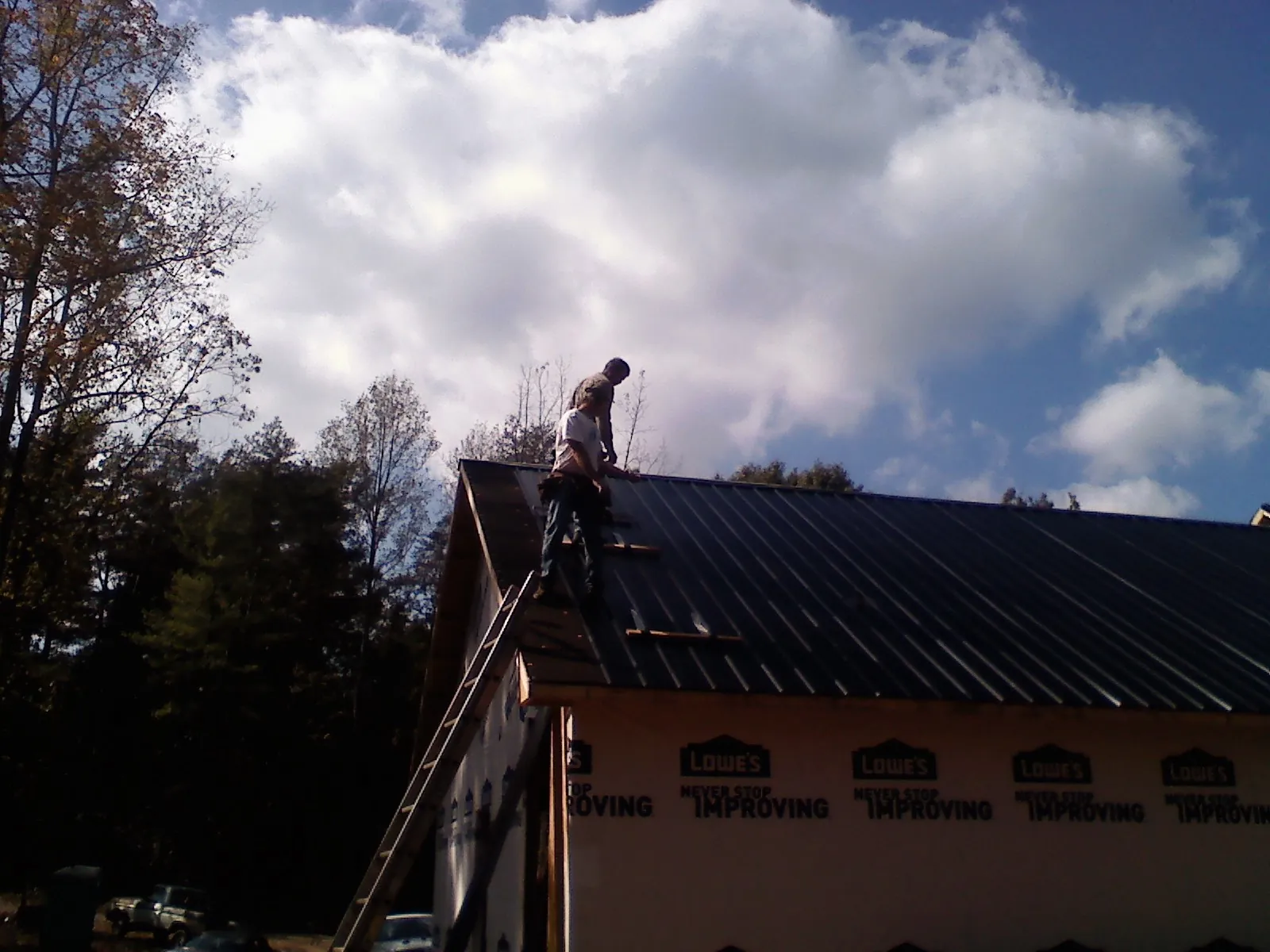Roofer fastening dark metal panels high against a cloudy sky, from a Roof Inspection job in Conneaut