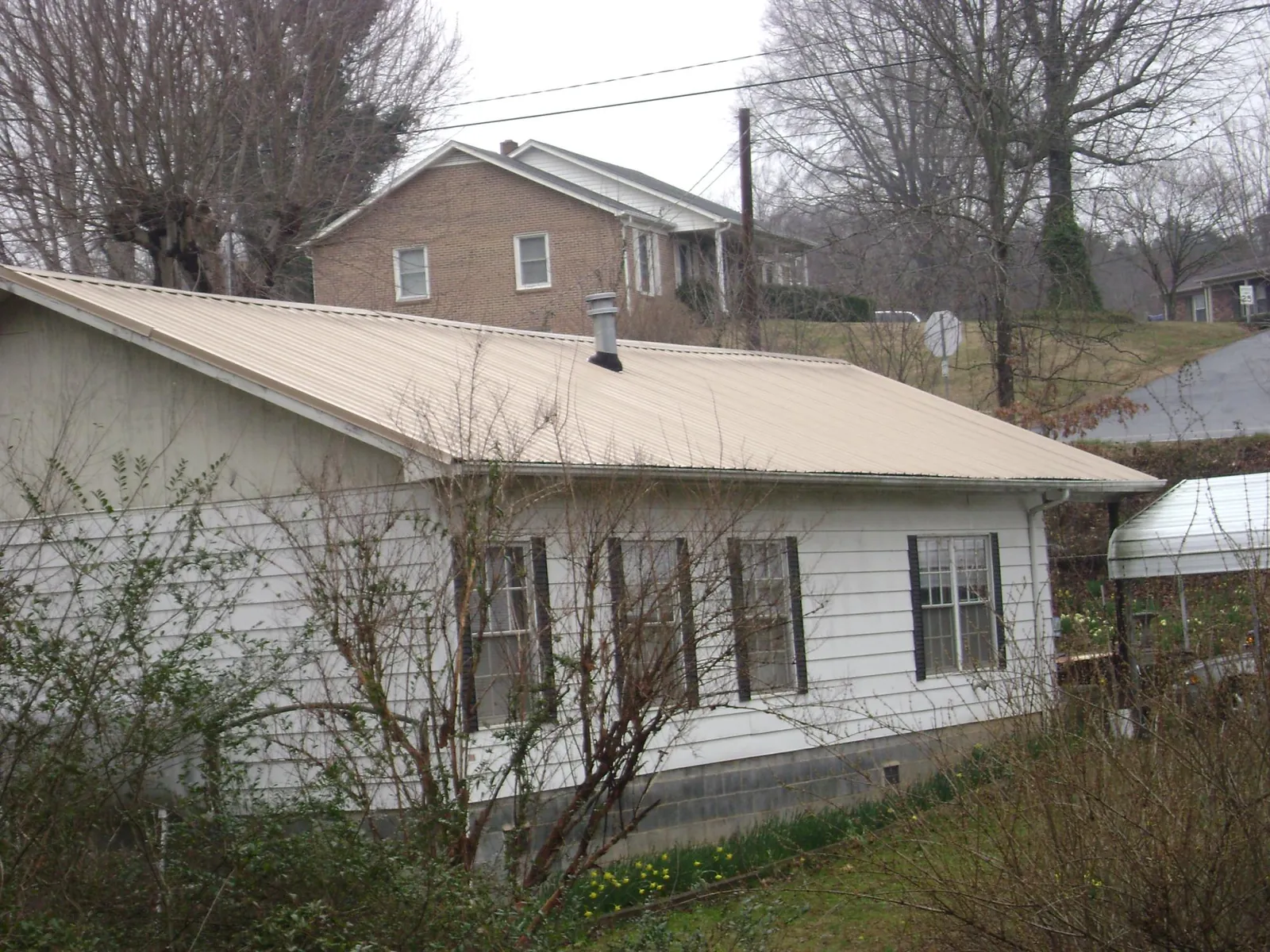 Tan metal roof on a white sided house set into a hillside — Commercial Roofing by Roofing Brothers in Conneaut