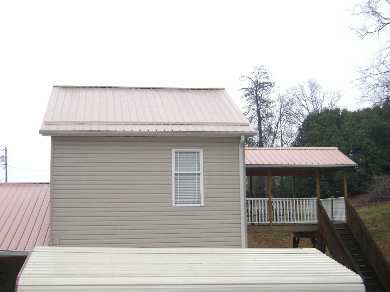 Tan metal roofs on a two story addition and attached porch, from a Roof Replacement job in Conneaut
